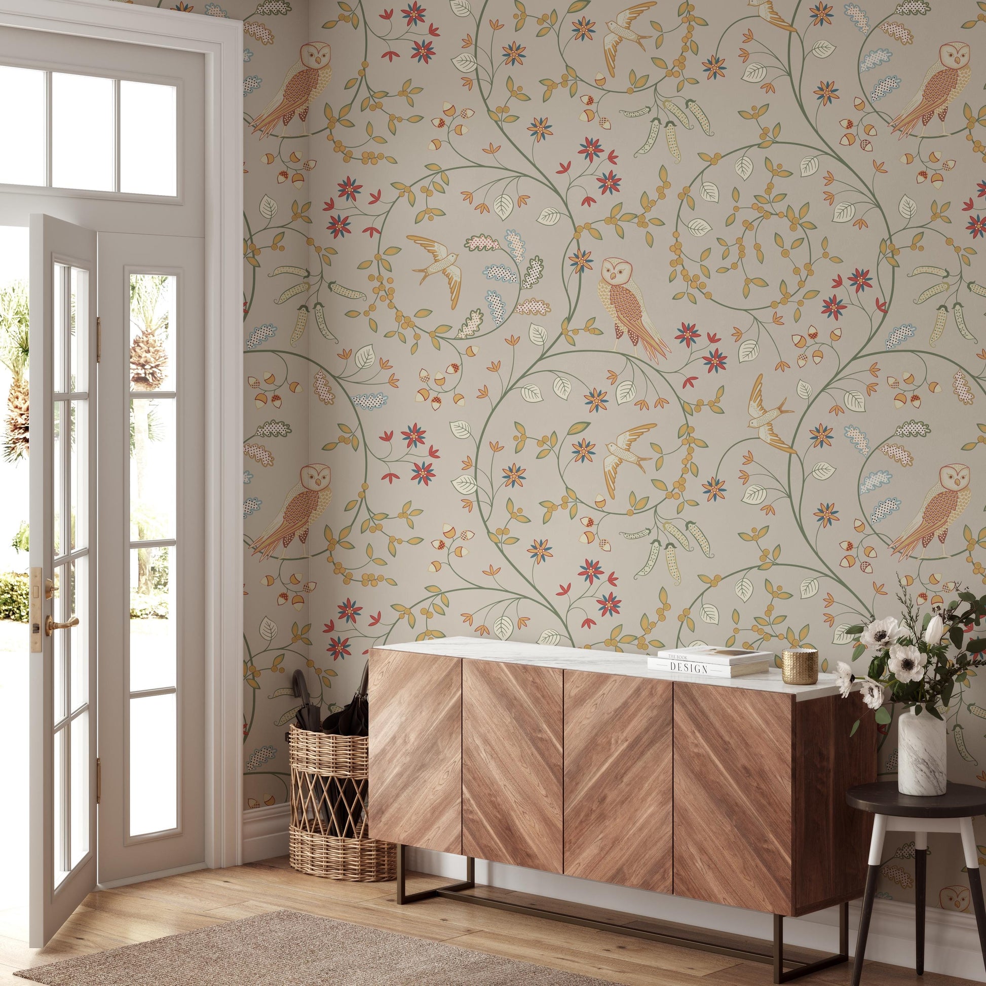 a room with a wooden cabinet, a wicker basket, and a vase of flowers. The walls are decorated with a floral wallpaper pattern, and there is a door with a window.