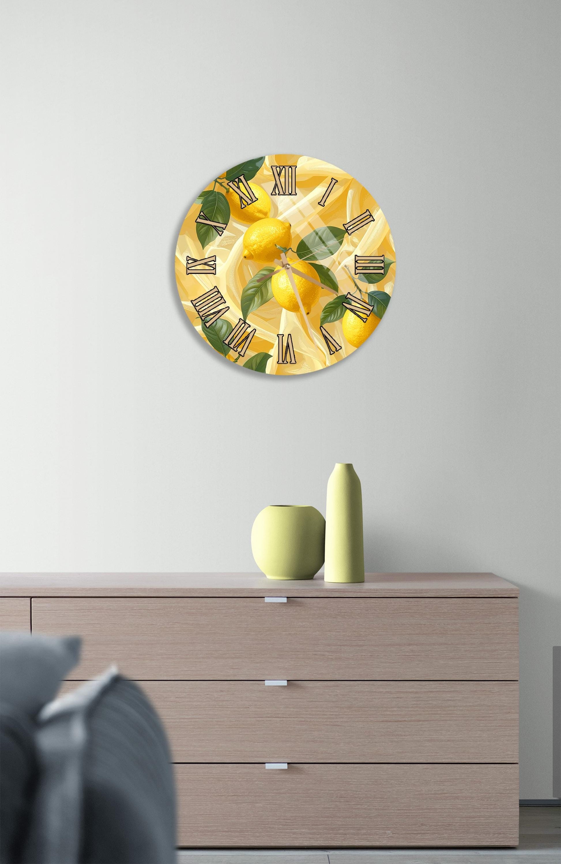 a wall clock with a design of lemons and leaves, mounted on a wall above a wooden dresser with a vase and a small sculpture on top.