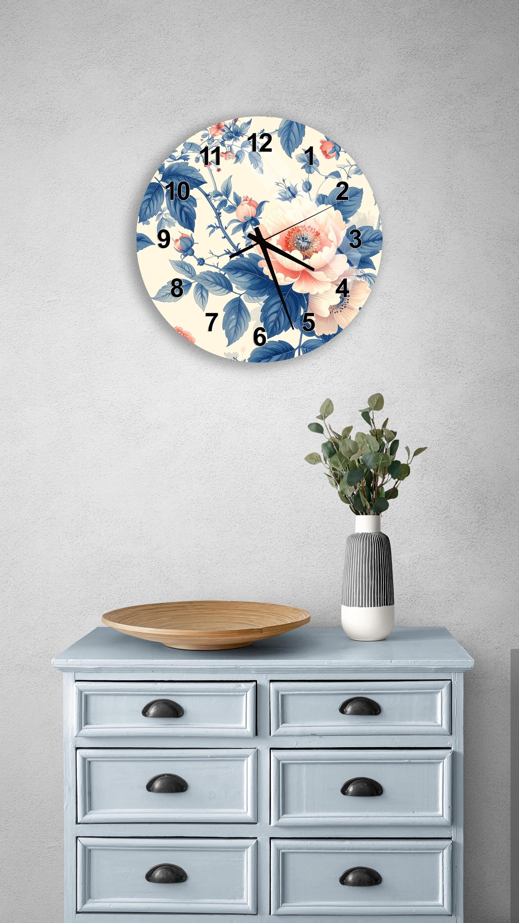 a wall clock with a floral design, a wooden tray, a vase with greenery, and a light blue dresser with six drawers.