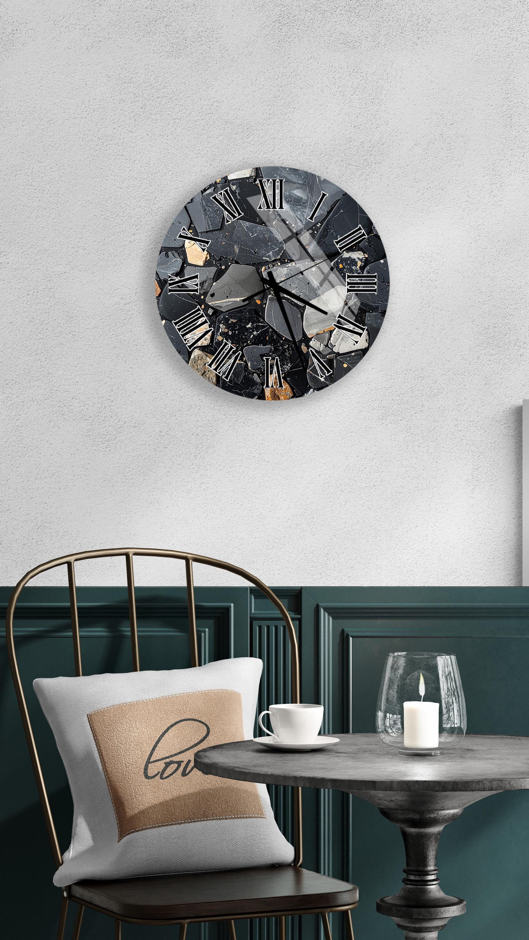 a modern black and white clock with a gold frame, mounted on a white wall above a black chair with a white pillow. The chair is positioned in front of a small round table with a white coffee cup and a lit candle on it.