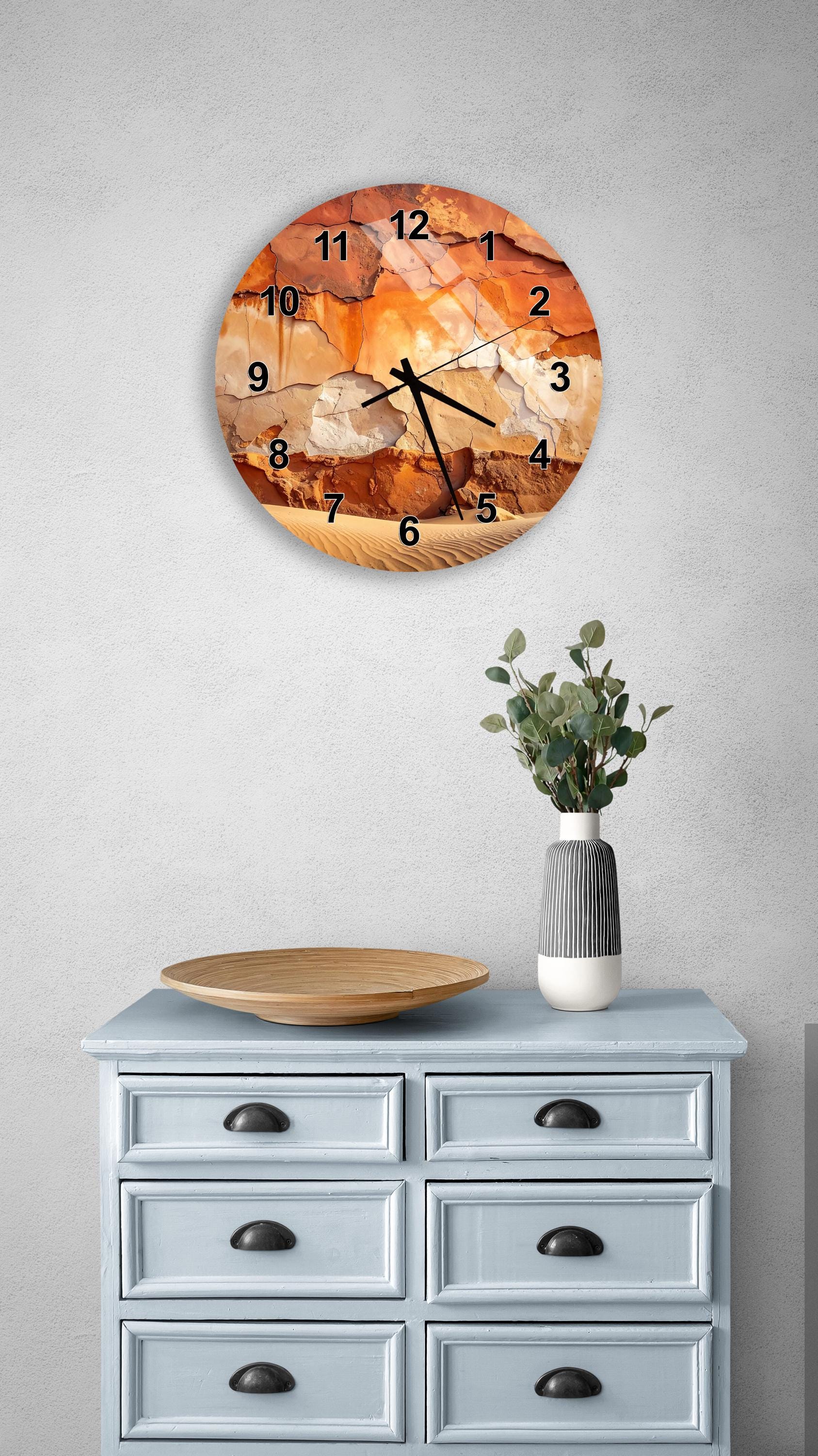 a wall clock with a unique stone-like design, mounted on a wall above a light blue dresser with six drawers. The dresser also has a vase with greenery on it, and there is a wooden plate on top of the dresser.