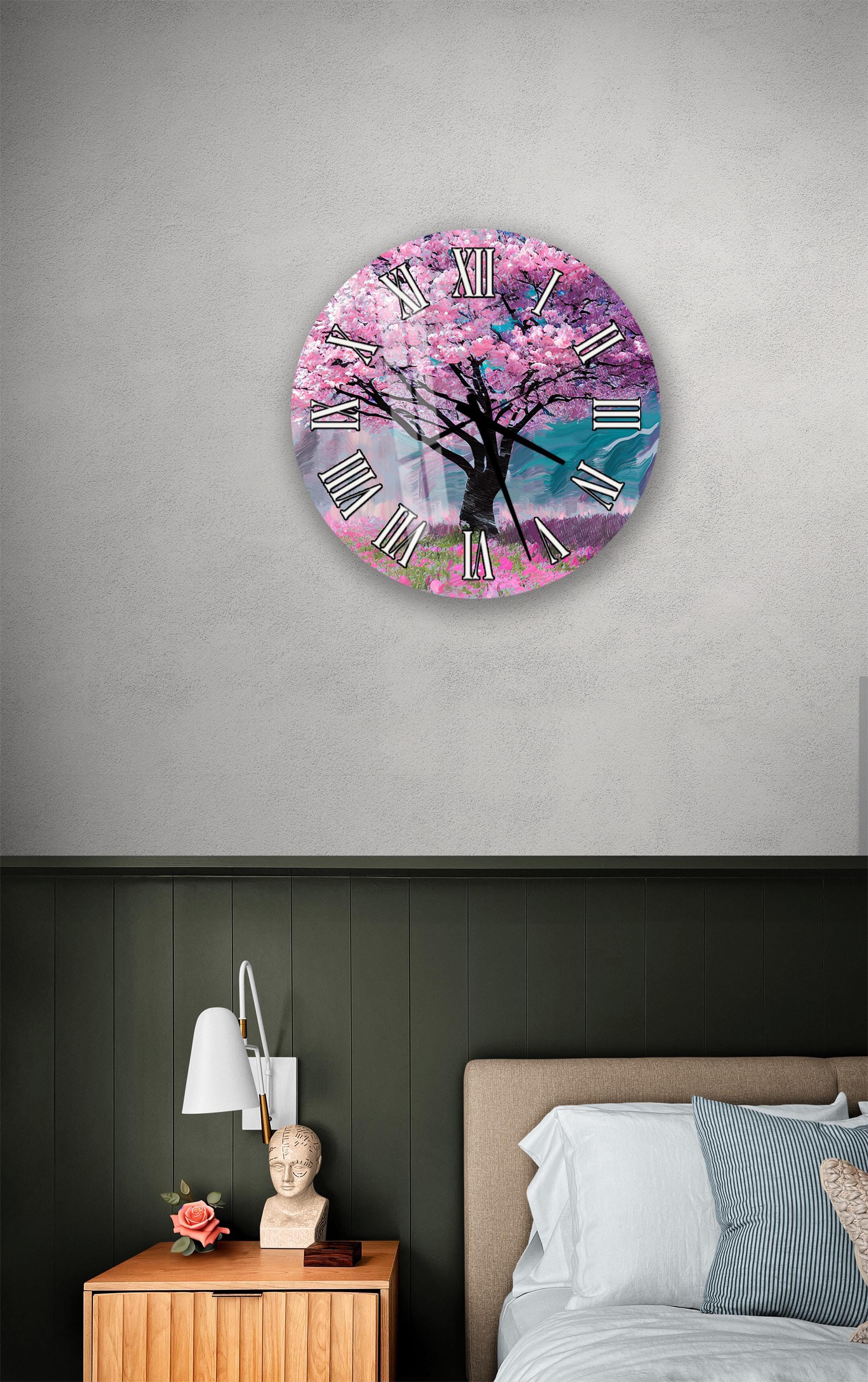 a clock with a pink tree design on it, mounted on a wall above a bedside table with a lamp and a small statue.