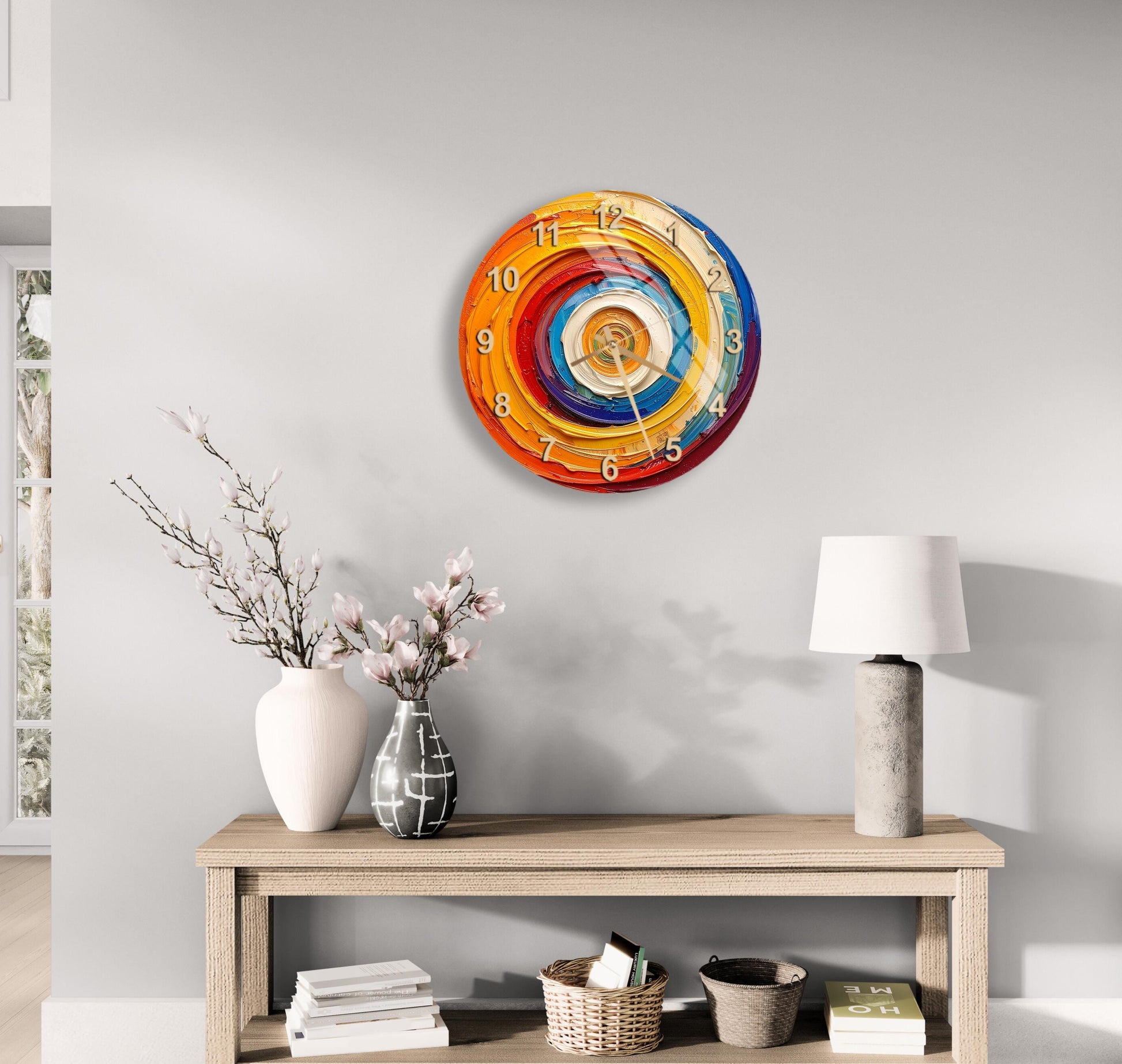 a wall clock with a colorful spiral design, a wooden table with a lamp, a vase with flowers, and some books on a shelf.