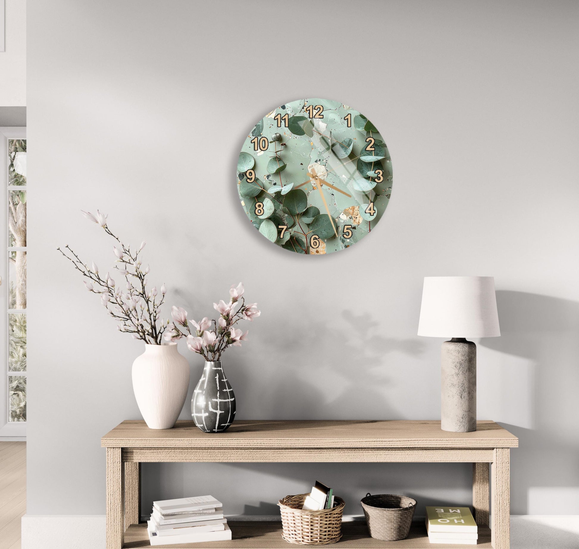 a modern living room with a round wall clock displaying a floral design, a wooden table with a lamp, a vase with pink flowers, and a stack of books.