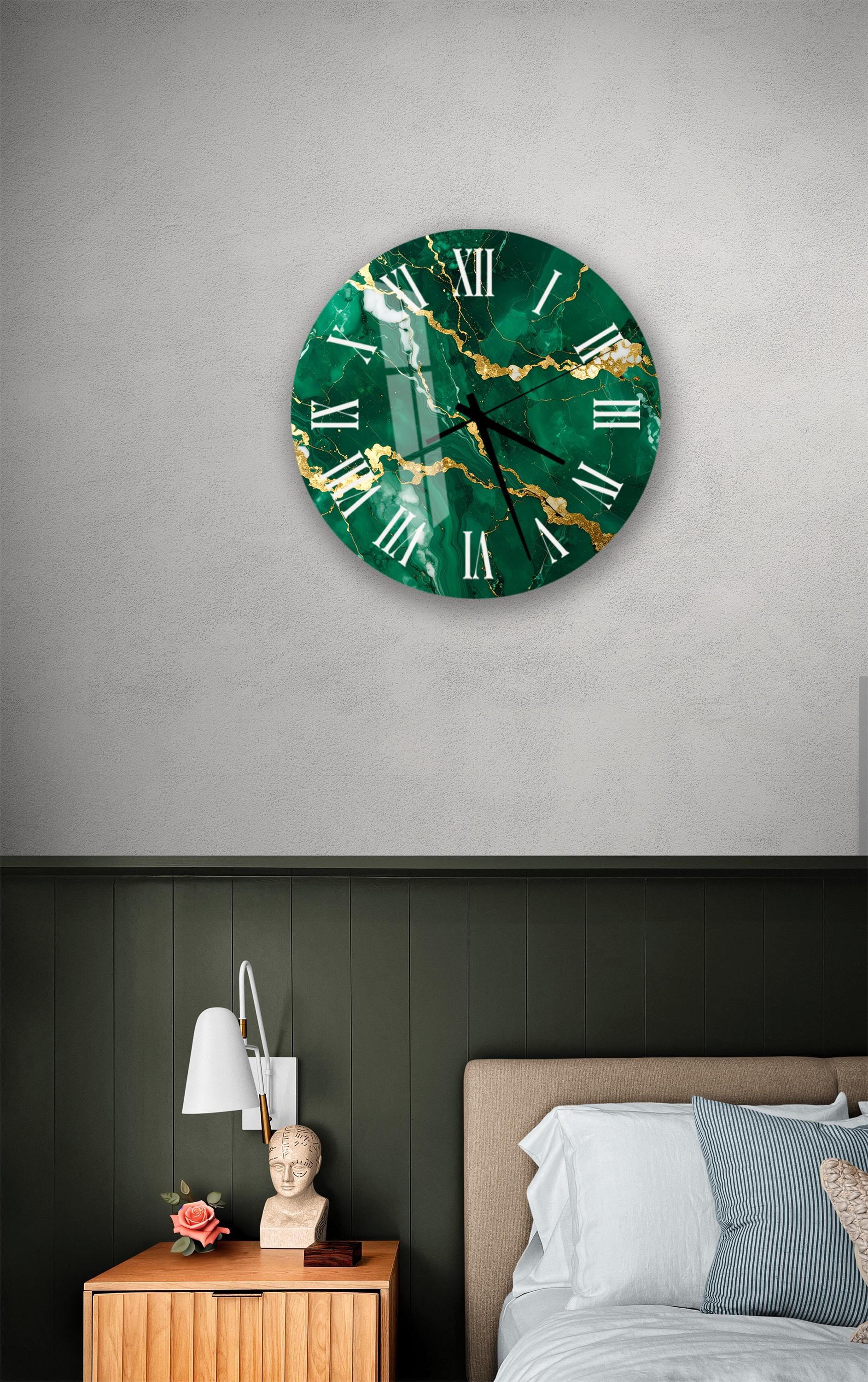 a bedroom setting with a large green marble clock hanging on the wall above a bed. The clock has a gold-colored design and appears to be made of a greenish material. The room has a dark green wall, a wooden nightstand with a lamp, and a bed with white sheets.