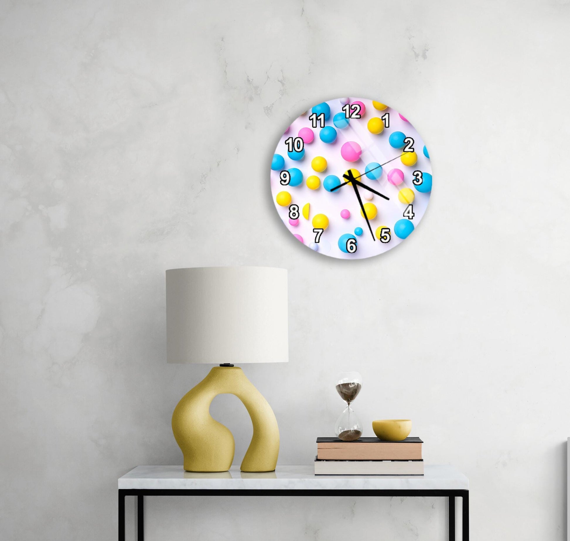 a wall clock with a colorful design, a yellow lamp on a table, and a stack of books on the table.