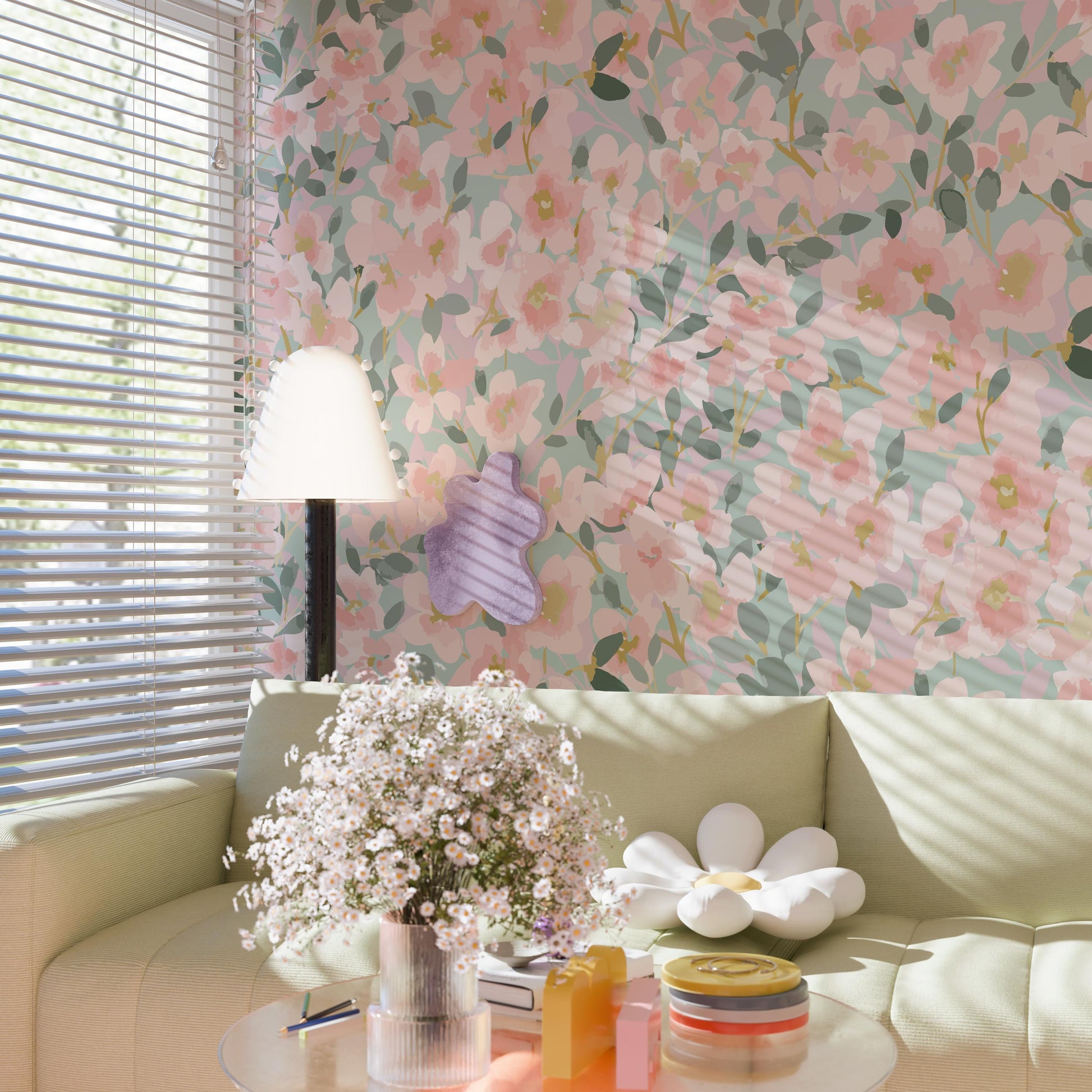 a cozy living room with a floral wallpaper, a white sofa, a lamp, a vase of white flowers, and a stack of books on a coffee table.