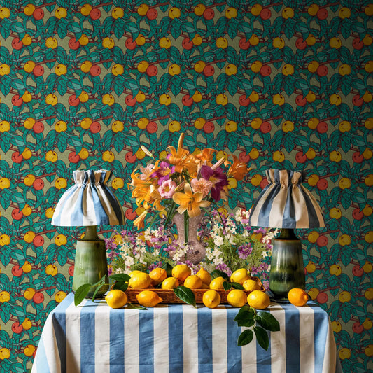 a table with a blue and white striped tablecloth, a vase of flowers, and a basket of lemons. The table is set against a wall with a pattern of green and yellow flowers.