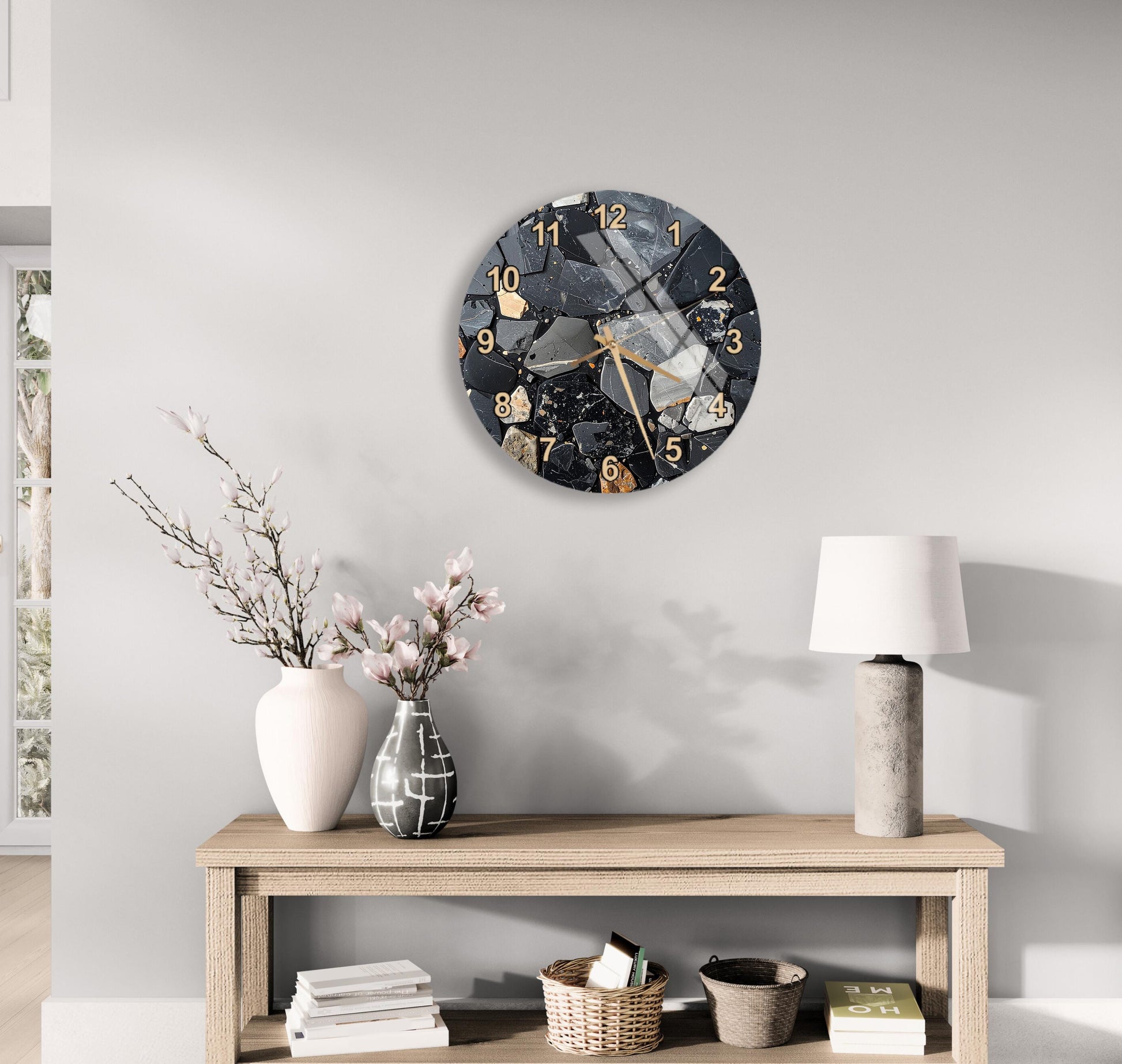 a modern clock with a black and white design, mounted on a wall above a wooden table with various decorative items, including a vase with flowers and a lamp.