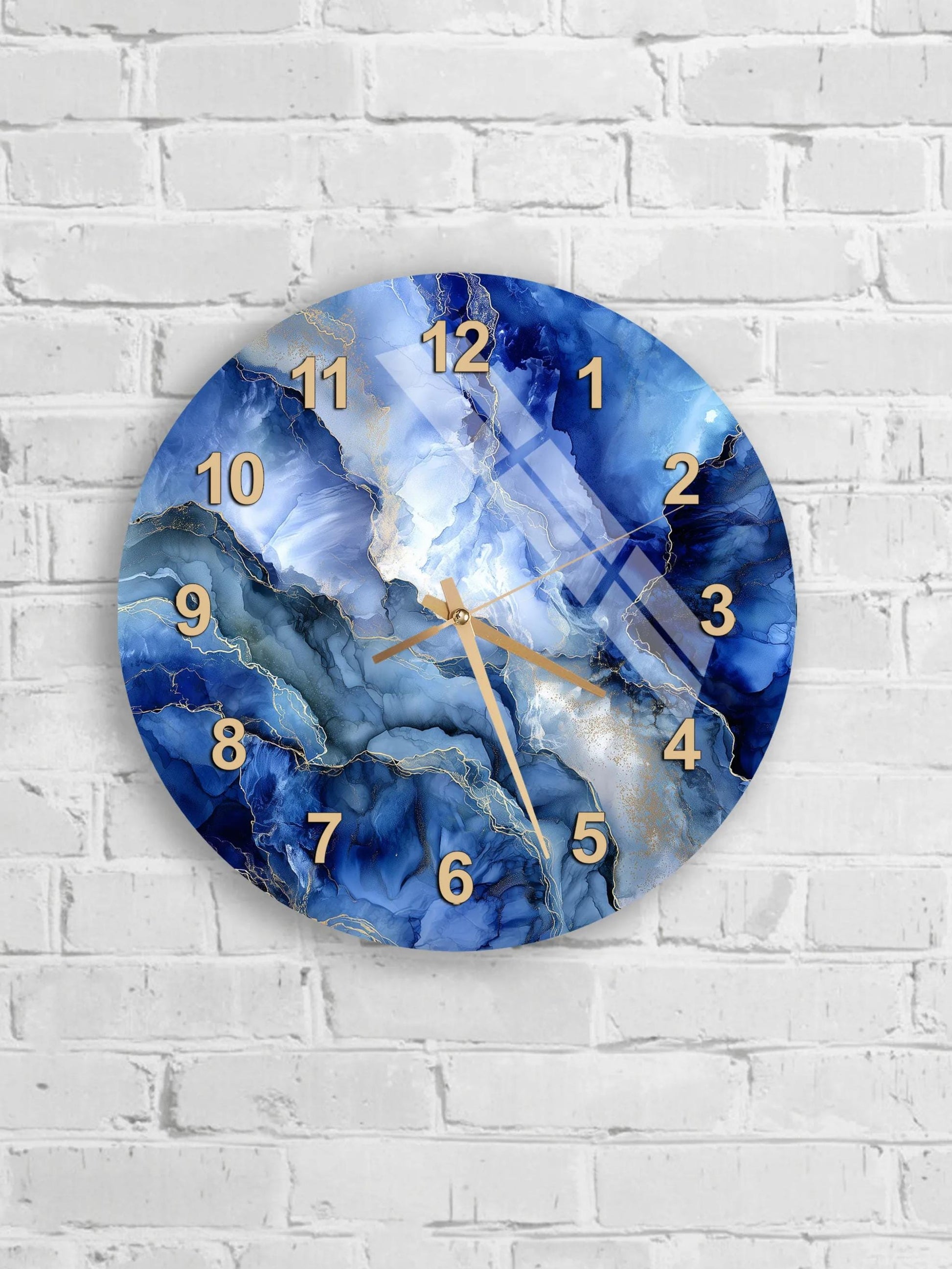 A wall clock with a blue marble-like design and gold numbers is mounted on a white brick wall.