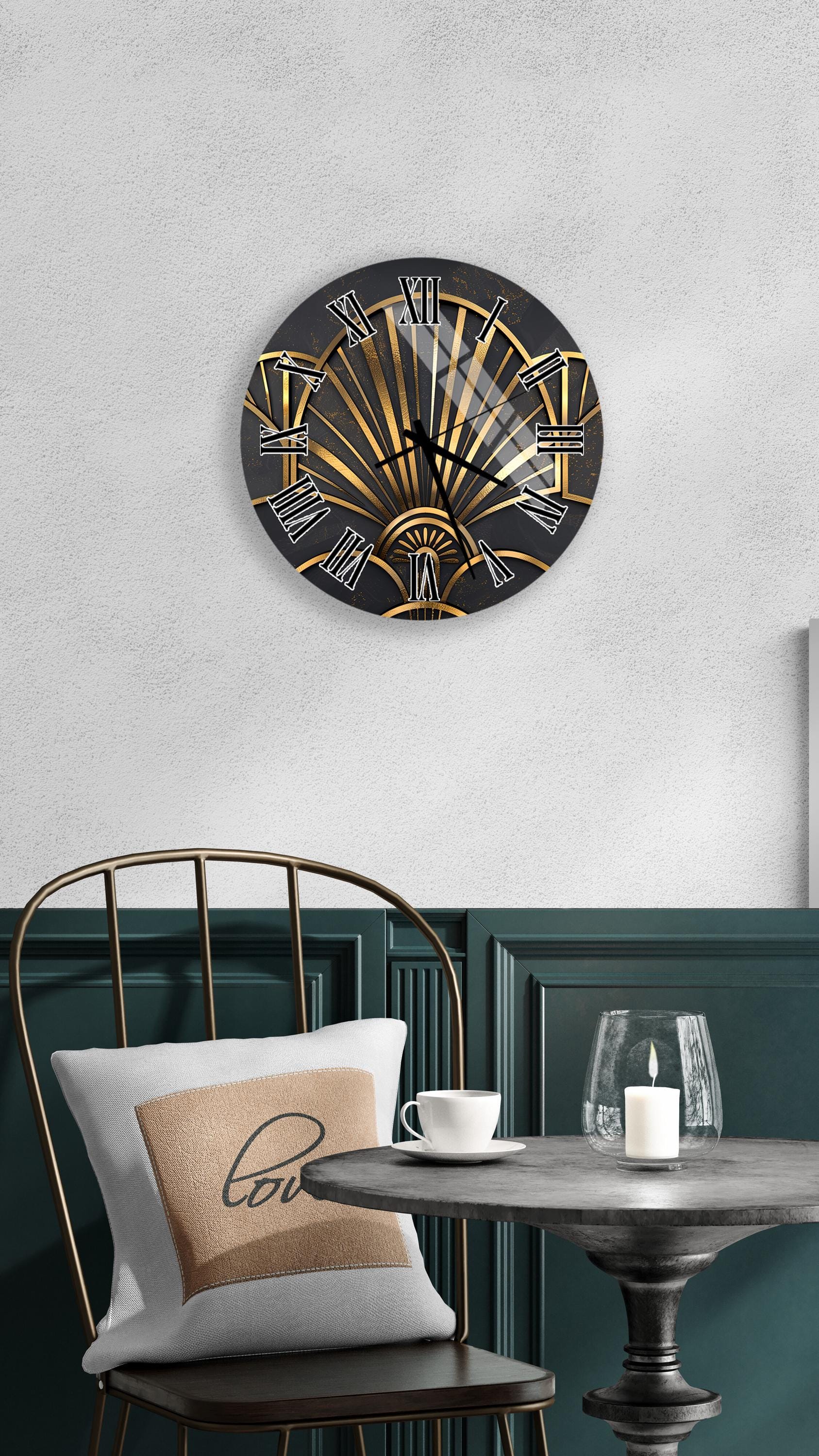a modern black and gold wall clock with an Art Deco design, mounted on a white wall above a black chair with a white pillow. In front of the chair, there is a small table with a glass and a candle, creating a cozy and stylish atmosphere.