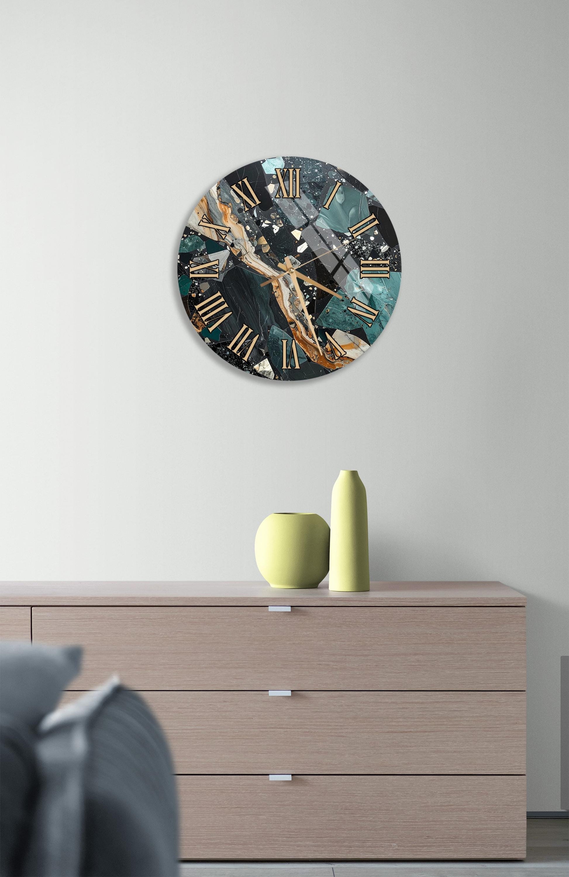 a modern clock with a marble-like design on a white wall, accompanied by a wooden dresser and a small yellow vase.