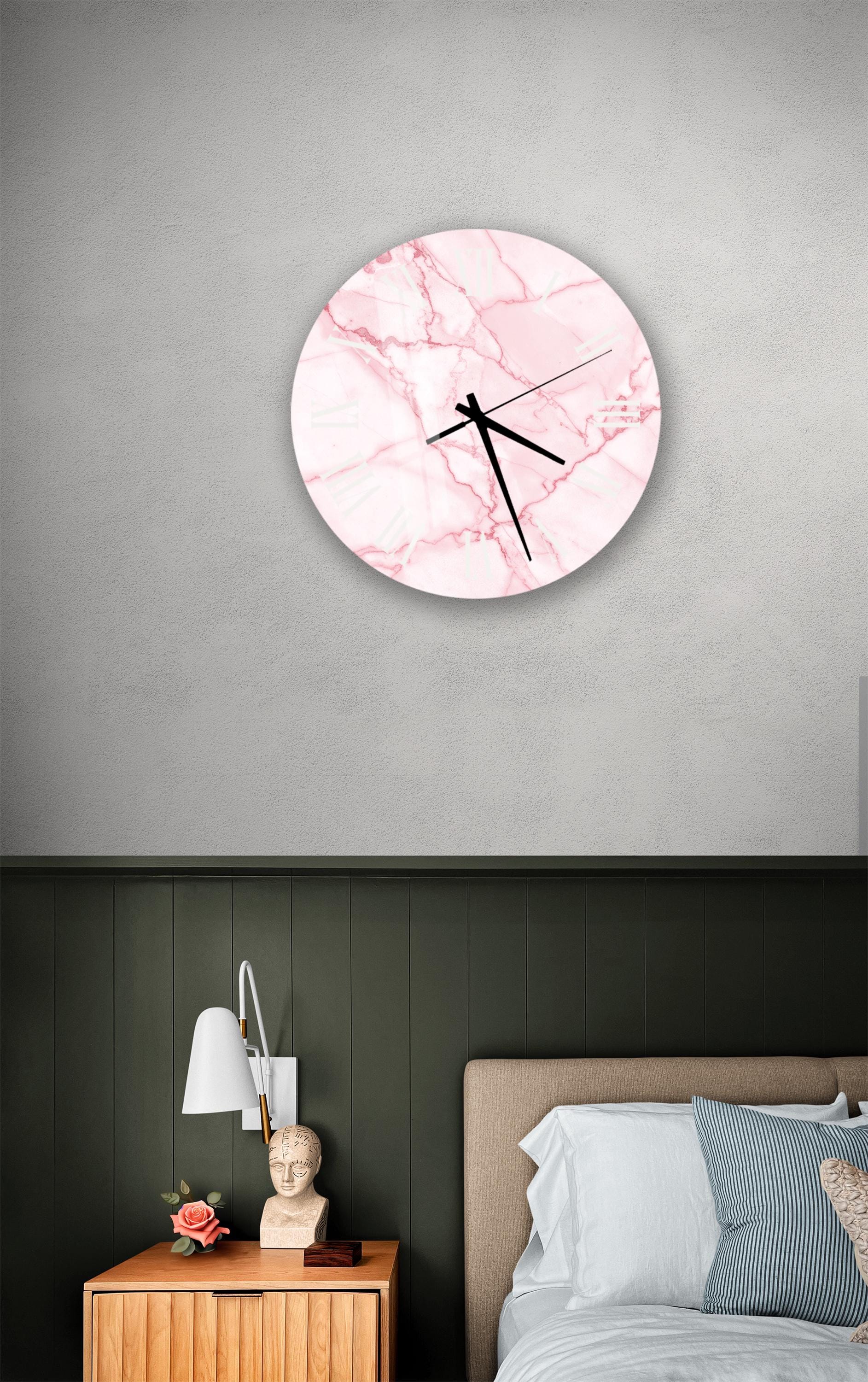 a bedroom setting with a round wall clock displaying a pink marble design, a wooden nightstand with a lamp, and a bed with white bedding.