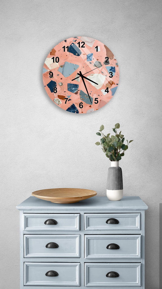 a round wall clock with a unique, colorful design, mounted on a wall above a light blue dresser with six drawers. The dresser also has a vase with greenery on it, and there is a wooden plate on top of it.