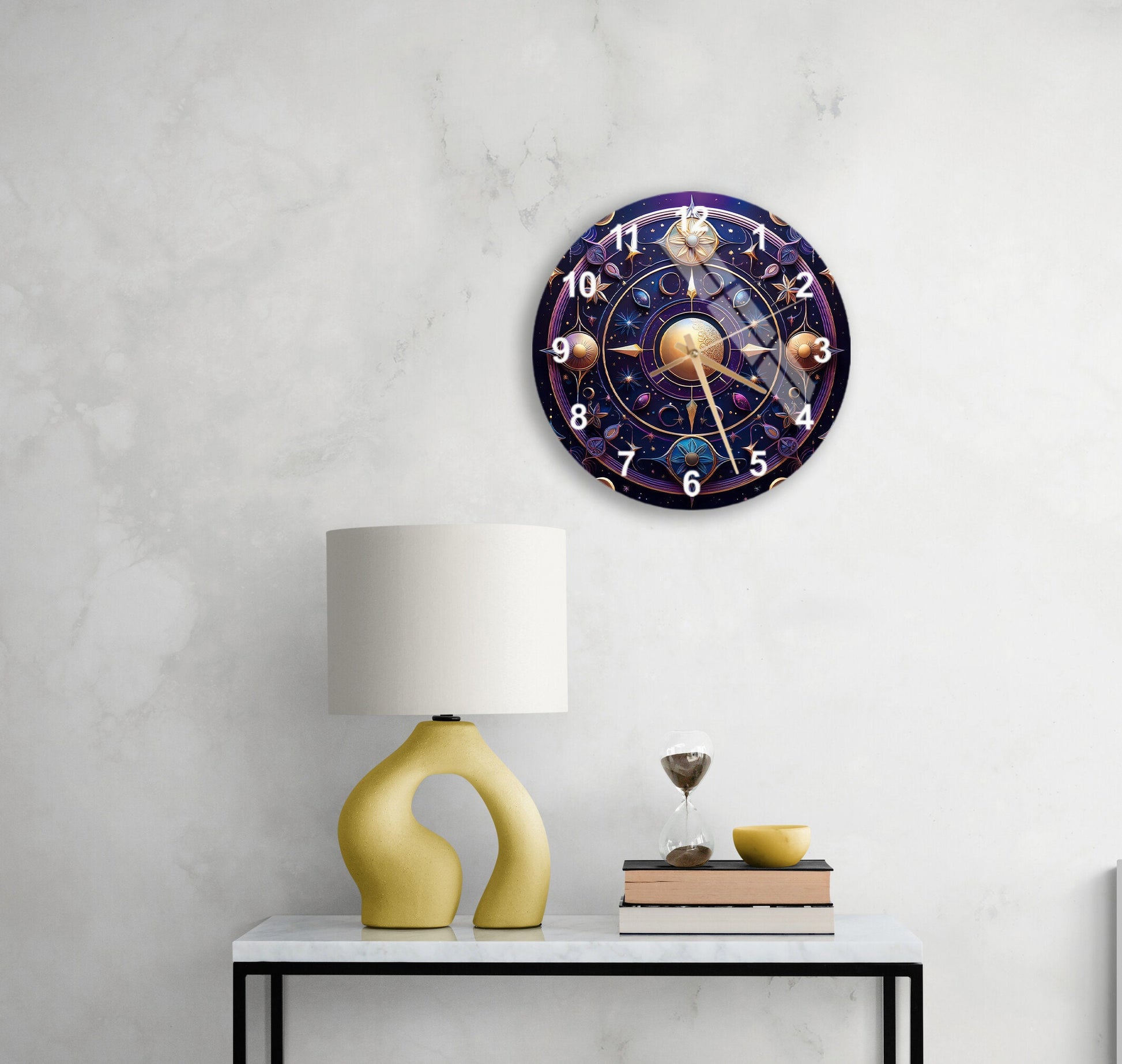 May include: A celestial-themed wall clock with gold and purple accents. The clock face features planets, stars, and celestial symbols. The numbers are clearly visible, and the clock hands are elegantly designed. The clock has a diameter of approximately 12 inches. The clock is displayed on a wall, above a table with a lamp and other decorative items. The overall style is modern and sophisticated, suitable for a home or office setting.