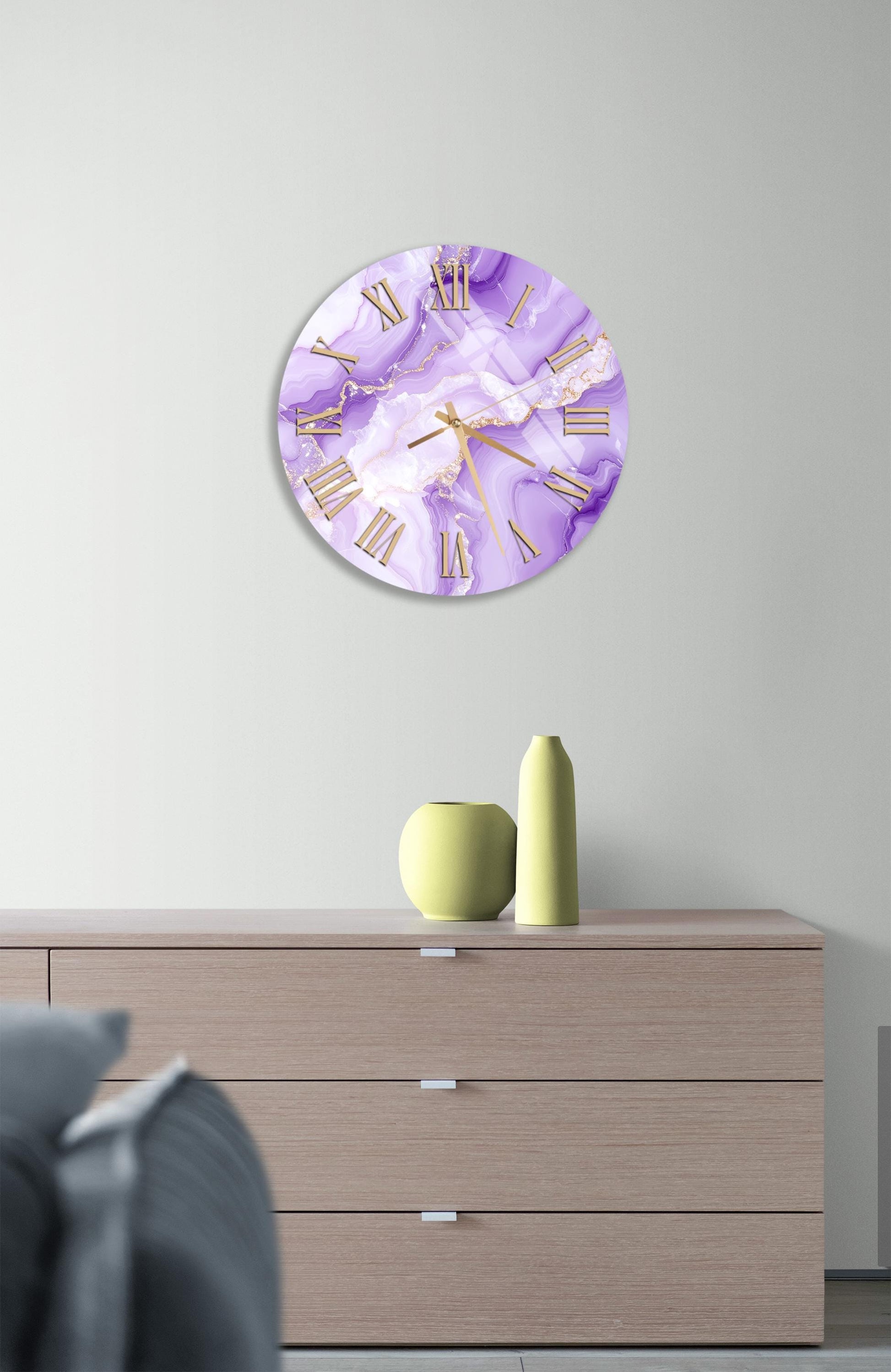 a wall clock with a purple and white marble design, mounted on a wall above a wooden dresser with three drawers.