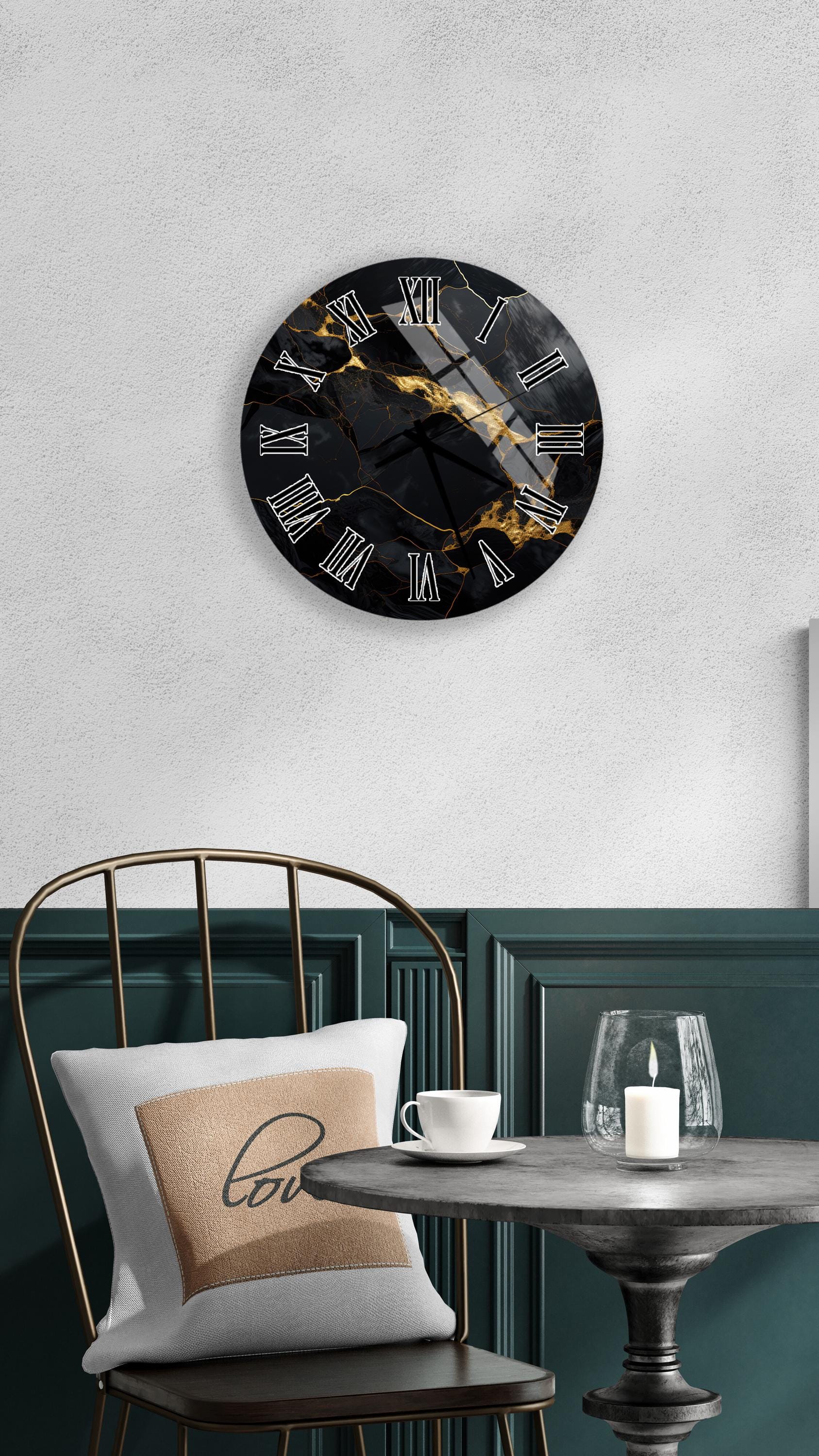 a modern black and gold wall clock with a marble-like design, mounted on a white wall above a black chair with a gold frame. The chair is positioned in front of a small round table with a white tablecloth, and a white candle is placed on the table.