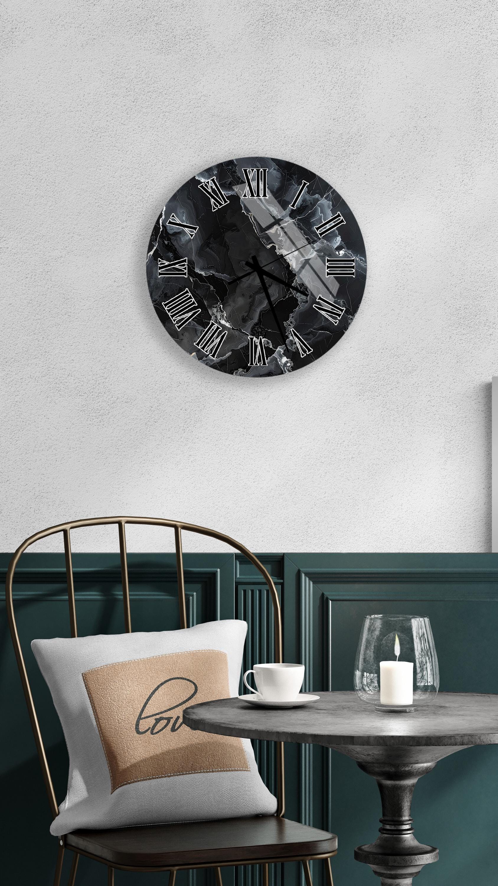 a modern black and white clock with a marble-like design, mounted on a white wall above a black metal chair. The chair is positioned in front of a green wall, and there is a small table with a white cup and a lit candle on it.