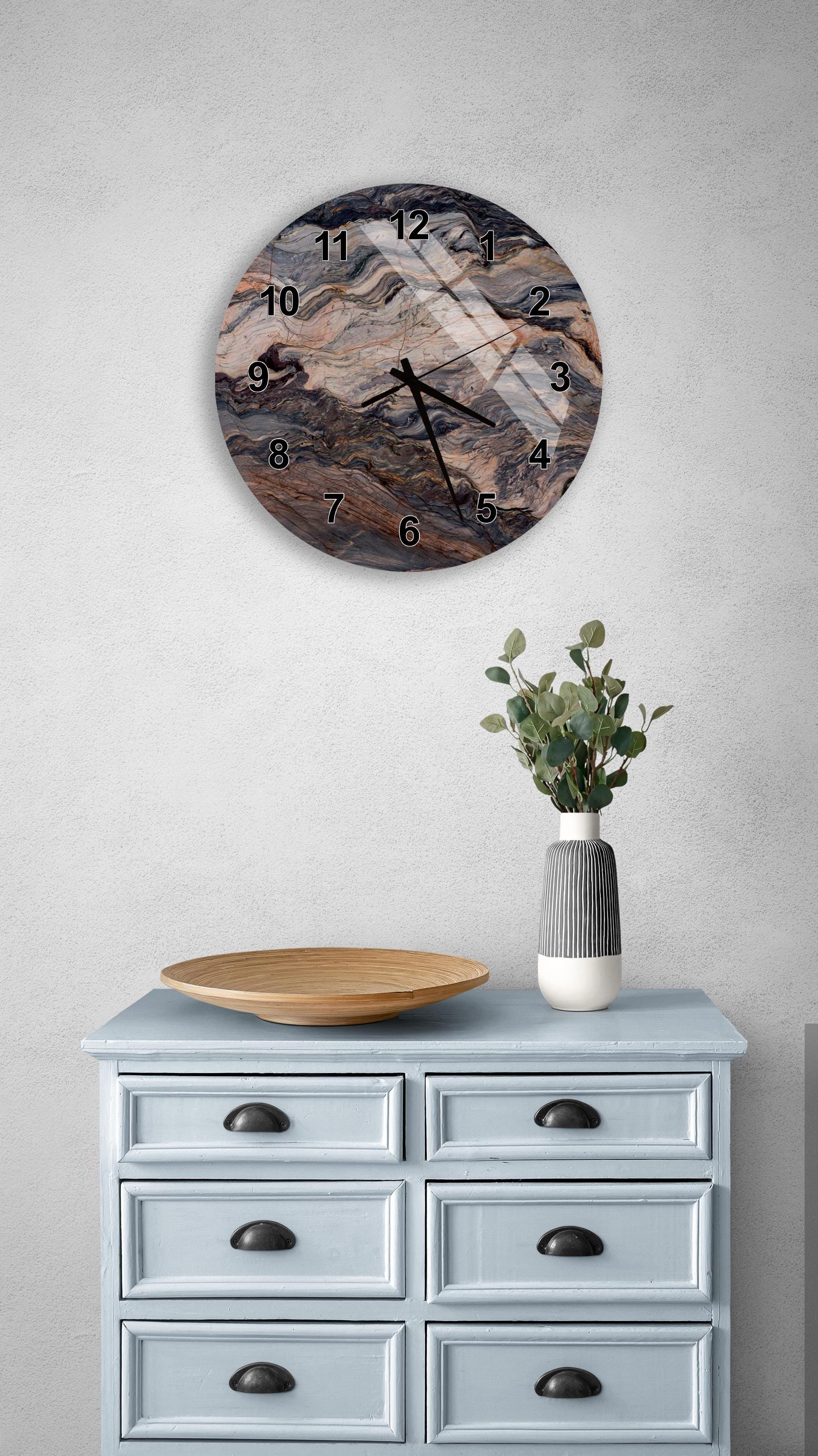 a wall clock with a marble-like design, mounted on a wall above a light blue dresser with six drawers. The dresser also has a wooden bowl and a vase with greenery on it.
