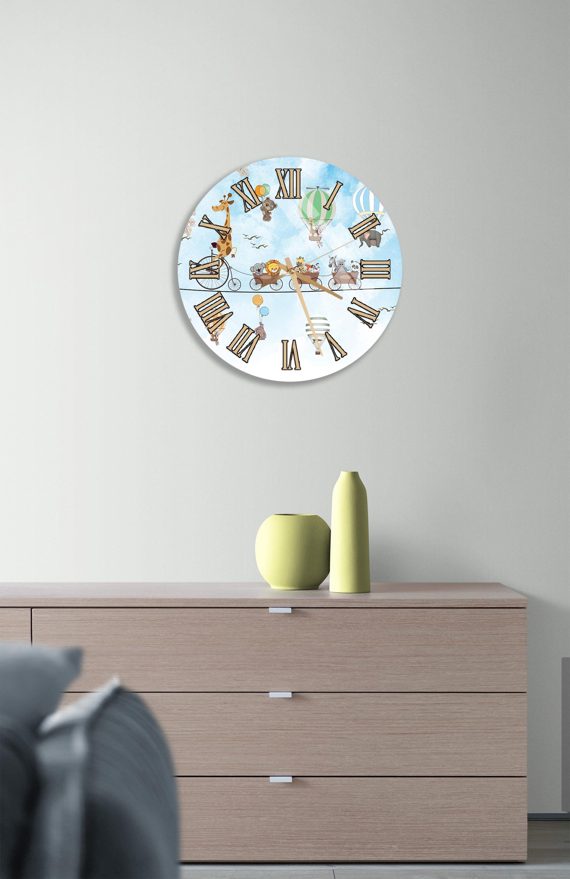 a round clock with a whimsical design, hanging on a wall above a wooden dresser.